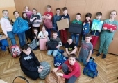 Grupa dziewiętnastu uczniów z klasy 3c z torbami na tle szafy. Na dole chłopiec z koszem.